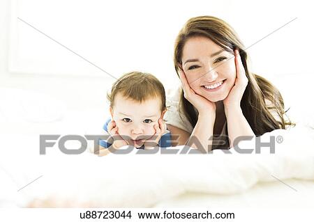 Picture - Mother and son (4-5) lying on bed and smiling. Fotosearch
