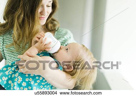 Picture - Mother feeding baby girl (12-17 months) in living room. Fotosearch