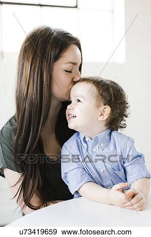 Stock Photo - Mother giving son (4-5) forehead kiss. Fotosearch