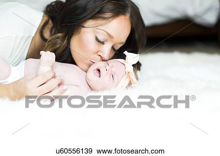 Stock Photo - Mother kissing daughter (0-1 months) on bed. Fotosearch