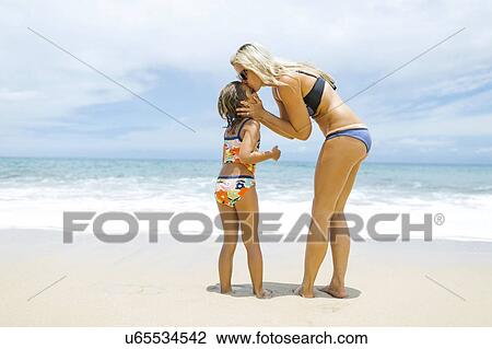 Stock Image - Mother kissing daughter (6-7) on beach. Fotosearch