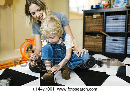 Stock Image - Mother learning son (4-5) to tie shoes. Fotosearch