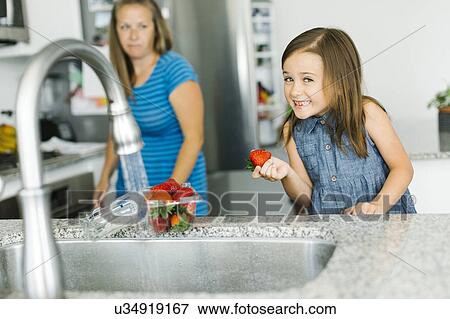 Mother looking at daughter (6-7) holding strawberry in kitchen View Large Photo Image Stock Photo - Mother looking at daughter (6-7) holding strawberry in kitchen. Fotosearch