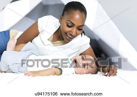 Stock Photograph - Mother lying down with baby boy (2-5 months) on floor. Fotosearch