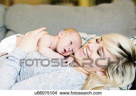 Picture - Mother lying on sofa and holding his one day son (0-1 months). Fotosearch