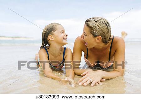 Stock Photo - Mother lying with daughter (6-7) on beach. Fotosearch