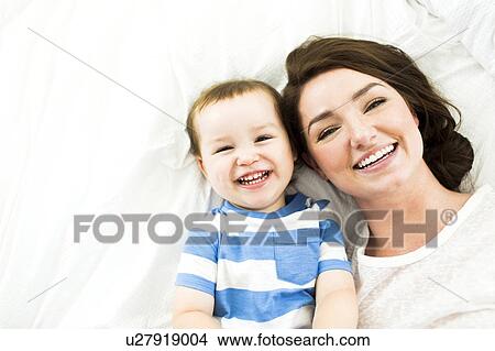 Picture - Mother lying with son (4-5) on bed and smiling. Fotosearch