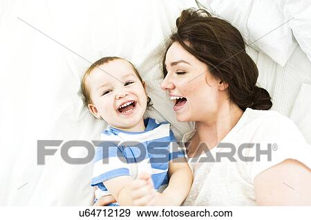 Mother lying with son (4-5) on bed and laughing View Large Photo Image Stock Photo - Mother lying with son (4-5) on bed and laughing. Fotosearch