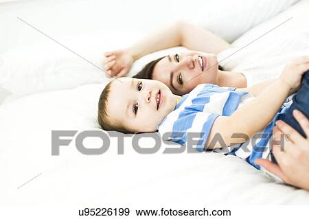 Stock Photo - Mother lying with son (4-5) on bed and smiling. Fotosearch