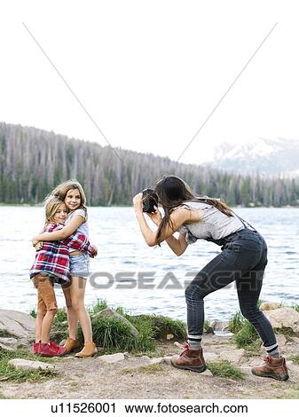 Stock Image - Mother photographing girl (8-9) and boy (6-7) by lake. Fotosearch