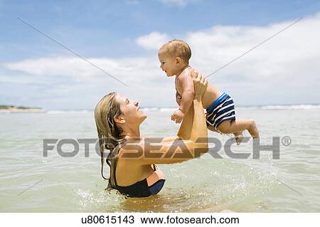 Stock Image - Mother playing with son (12-17 months) in sea. Fotosearch