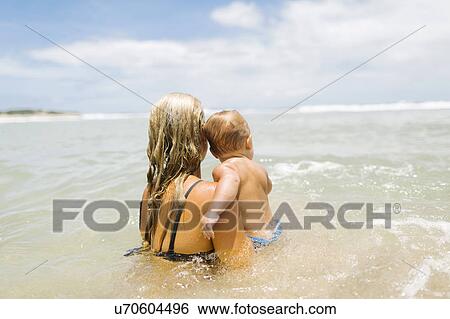 Stock Photograph - Mother playing with son (12-17 months) in sea. Fotosearch