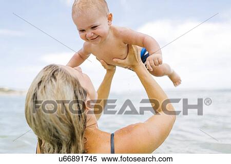 Stock Photography - Mother playing with son (12-17 months) in sea. Fotosearch