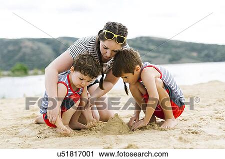 Stock Image - Mother playing with sons (4-5, 6-7) on beach by lake. Fotosearch