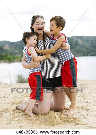Stock Photography - Mother playing with sons (4-5, 6-7) on beach by lake. Fotosearch