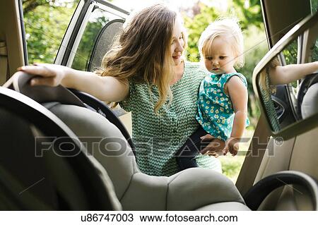 Stock Image - Mother preparing baby girl (12-17 months) for car trip. Fotosearch