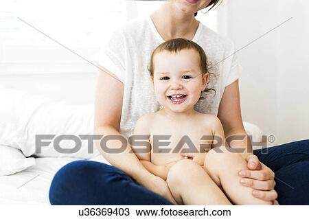 Stock Image - Mother sitting with son (4-5) on bed. Fotosearch