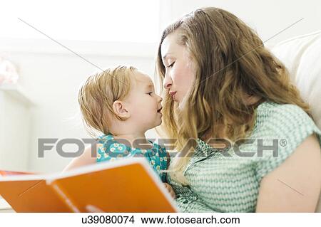 Picture - Mother with baby girl (12-17 months) sitting in living room and reading book. Fotosearch