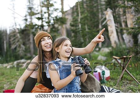 Stock Image - Mother with daughter (8-9) using binoculars in forest. Fotosearch