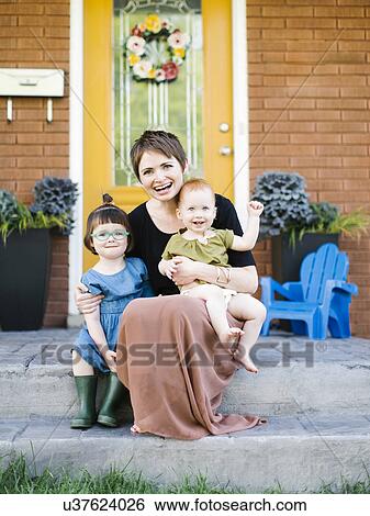 Stock Photograph - Mother with daughters (2-3, 12-17 months) sitting in front of house. Fotosearch