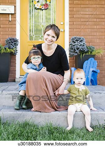 Stock Photography - Mother with daughters (2-3, 12-17 months) sitting in front of house. Fotosearch