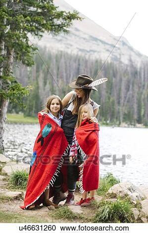 Stock Image - Mother with kids (6-7, 8-9) wrapped in blanket standing by lake. Fotosearch