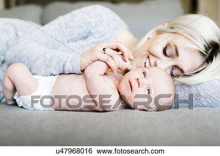 Stock Photograph - Mother with newborn (0-1 months) lying on sofa. Fotosearch