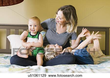 Mother with sons (12-17 months, 4-5) sitting on bed View Large Photo Image Stock Photo - Mother with sons (12-17 months, 4-5) sitting on bed. Fotosearch