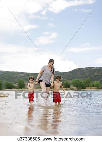 Stock Photograph - Mother with sons (4-5, 6-7) wading in lake. Fotosearch