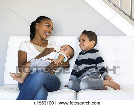 Stock Image - Mother with two sons (2-5 months, 2-3) on sofa. Fotosearch