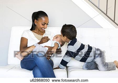 Stock Image - Mother with two sons (2-5 months, 2-3) on sofa. Fotosearch