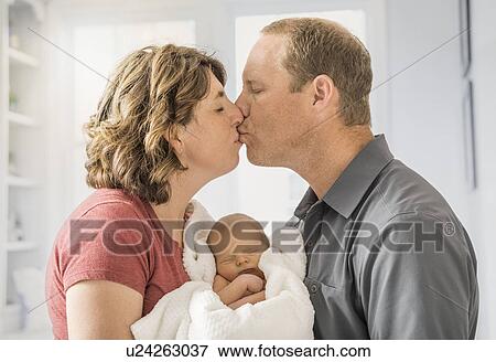 Parents holding and baby son (0-1 months) and kissing each other View Large Photo Image Stock Photo - Parents holding and baby son (0-1 months) and kissing each other. Fotosearch