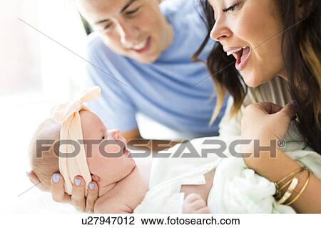 Stock Image - Parents lying on bed with daughter (0-1 months). Fotosearch