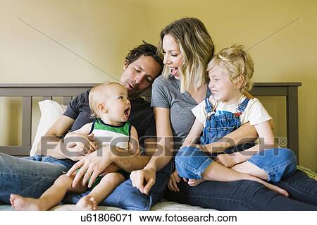 Stock Image - Parents playing with sons (12-17 months, 4-5) on bed. Fotosearch