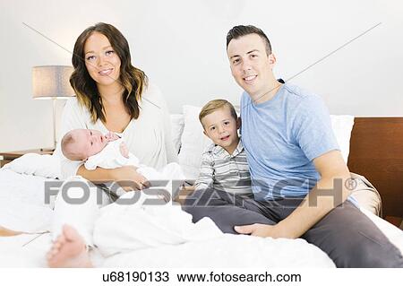 Stock Image - Parents sitting with daughter(0-1 months) and son (4-5) on bed in bedroom. Fotosearch
