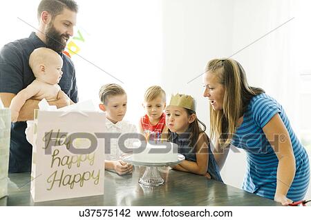 Stock Image - Parents with children (6-11 months, 2-3, 6-7) looking at daughter (6-7) blowing birthday candles. Fotosearch