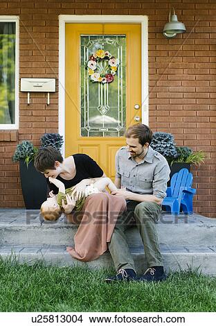 Picture - Parents with daughter (12-17 months) sitting in front of house. Fotosearch