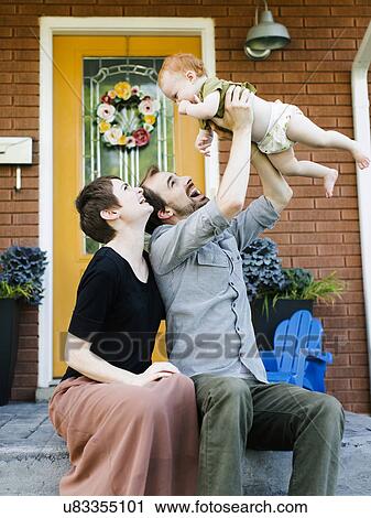 Stock Image - Parents with daughter (12-17 months) sitting in front of house. Fotosearch