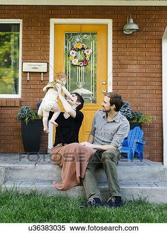 Stock Photography - Parents with daughter (12-17 months) sitting in front of house. Fotosearch