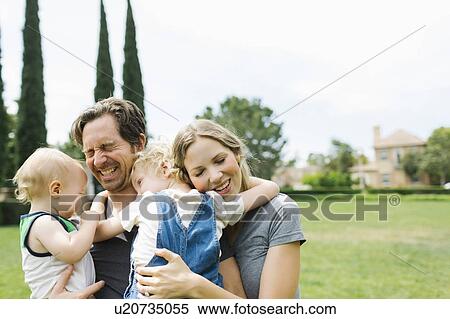 Stock Photography - Parents with sons (12-17 months, 4-5) embracing in park. Fotosearch