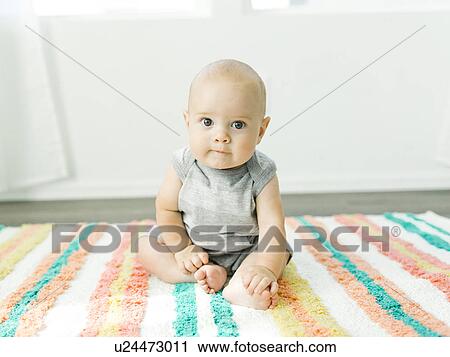 Stock Image - Portrait of baby boy (6-11 months) sitting on colorful carpet. Fotosearch