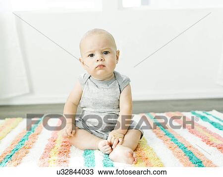 Stock Image - Portrait of baby boy (6-11 months) sitting on colorful carpet. Fotosearch