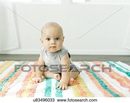 Stock Image - Portrait of baby boy (6-11 months) sitting on colorful carpet. Fotosearch