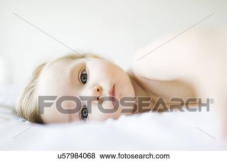 Stock Photo - Portrait of baby girl (6-11 months) lying on bed. Fotosearch