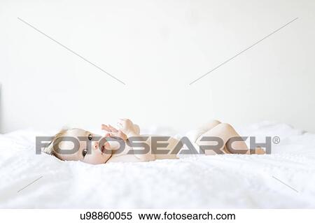 Stock Photography - Portrait of baby girl (6-11 Months) lying down on bed. Fotosearch