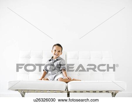 Stock Image - Portrait of boy (2-3) sitting on white sofa. Fotosearch