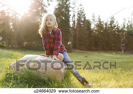 Stock Photo - Portrait of boy (6-7) sitting on rock in forest. Fotosearch