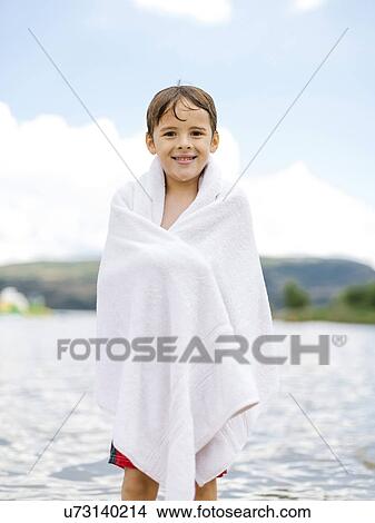 Picture - Portrait of boy (6-7) wrapped in towel standing by lake. Fotosearch