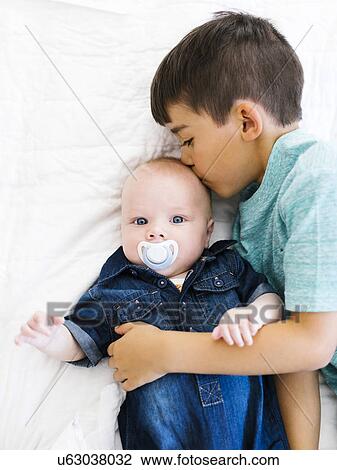 Stock Image - Portrait of boy (8-9) kissing his younger brother (12- 17 months). Fotosearch
