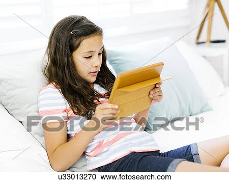Portrait of content girl (10-11) reclining on bed and using tablet View Large Photo Image Stock Image - Portrait of content girl (10-11) reclining on bed and using tablet. Fotosearch